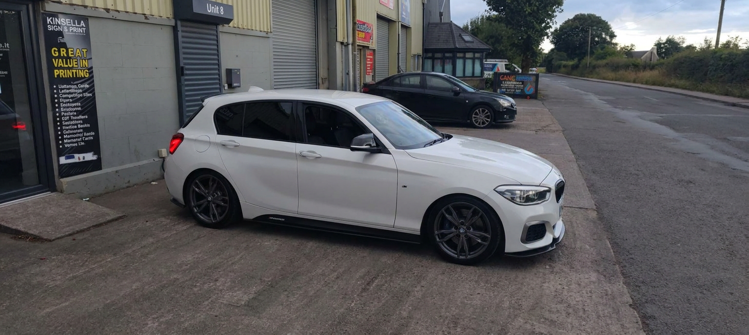 Front-right side profile of a white BMW 1 Series with dark tinted rear glass outside the workshop
