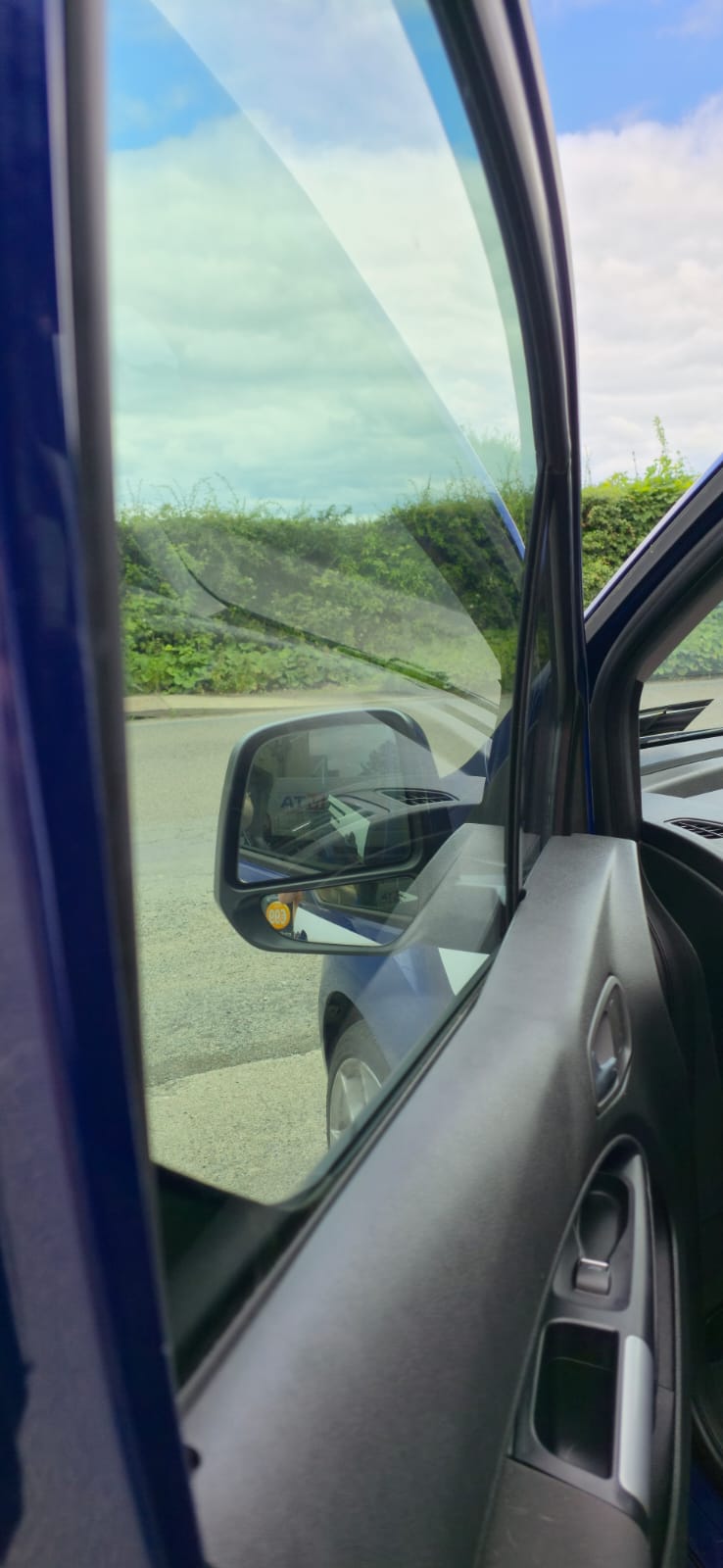 Front door glass of a blue Ford with a light legal-shade tint, seen from the driver's seat